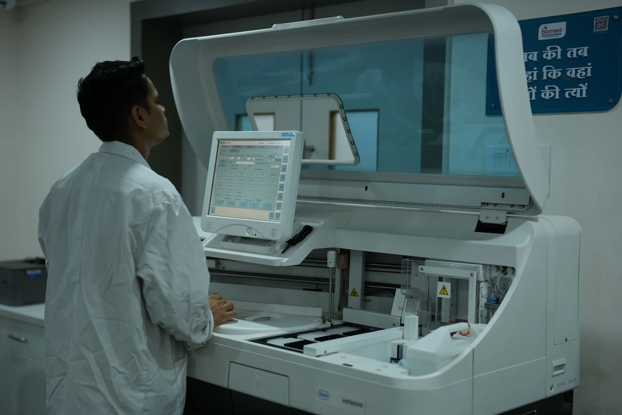 Laboratory technician at an analyser in a hospital laboratory, where a paper request becomes a recorded order