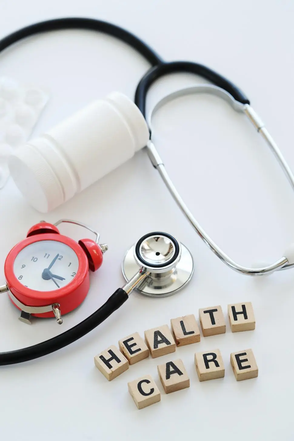 Stethoscope, medicine bottle and alarm clock beside wooden blocks spelling health care