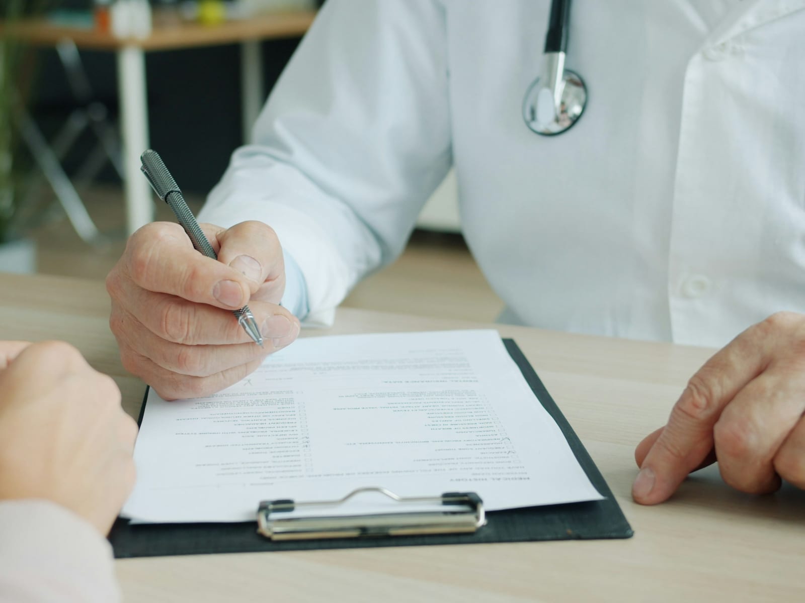 Doctor's hands writing consultation notes across the desk from a patient