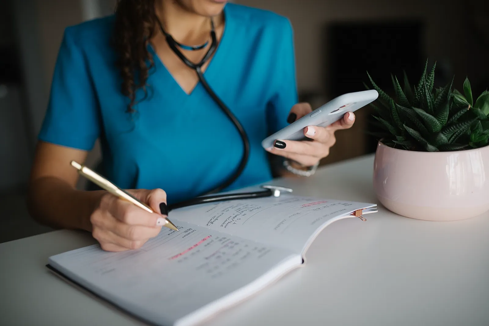 A doctor checking appointments on a smartphone while writing notes